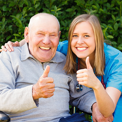 Elderly man and a young female caregiver both giving the thumbs-up